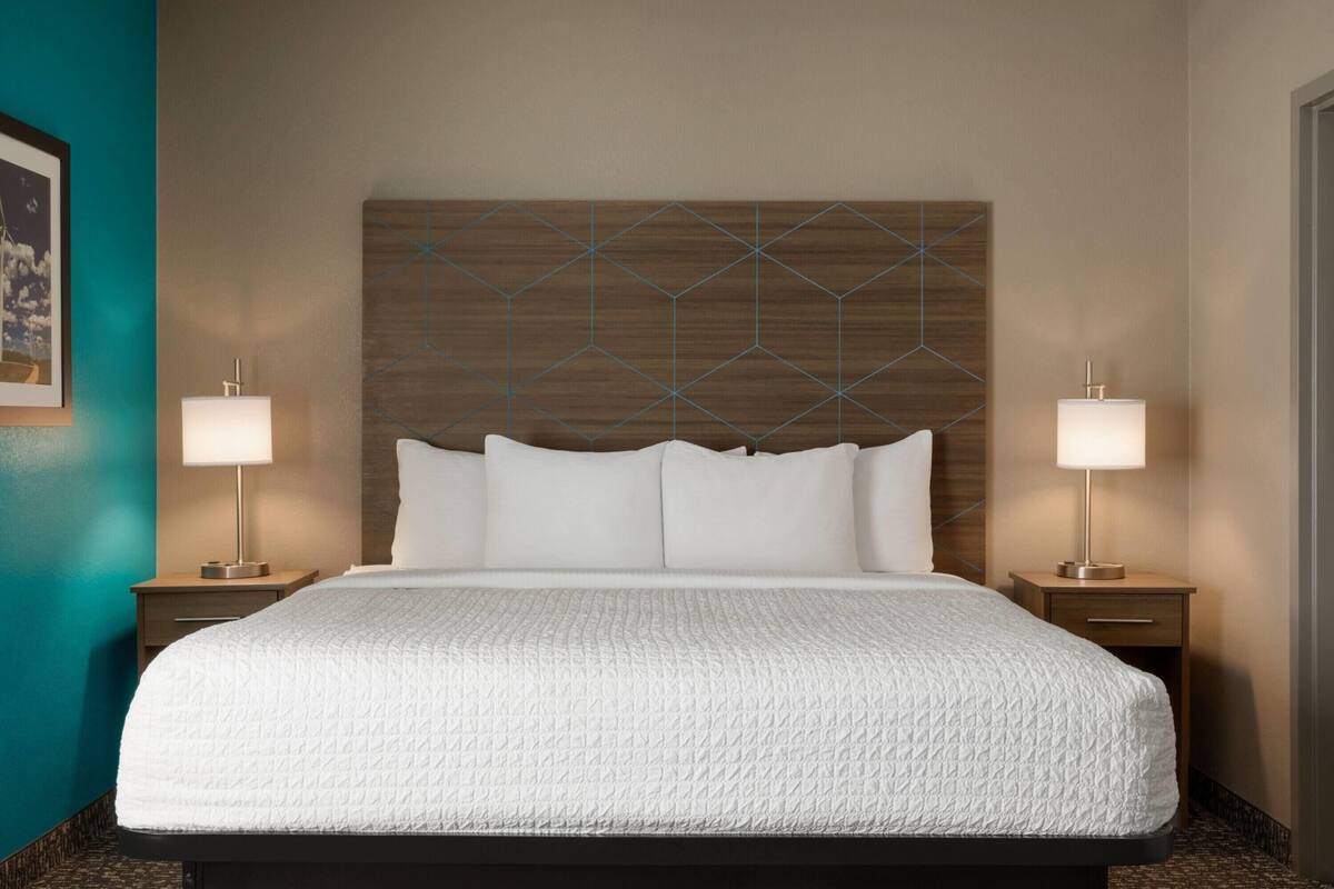 A hotel room with a large bed, two bedside tables with lamps, a wooden headboard, and a teal accent wall.