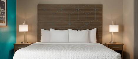 A hotel room with a large bed, two bedside tables with lamps, a wooden headboard, and a teal accent wall.