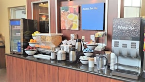 A breakfast bar with a coffee machine, juice dispenser, and various food items.