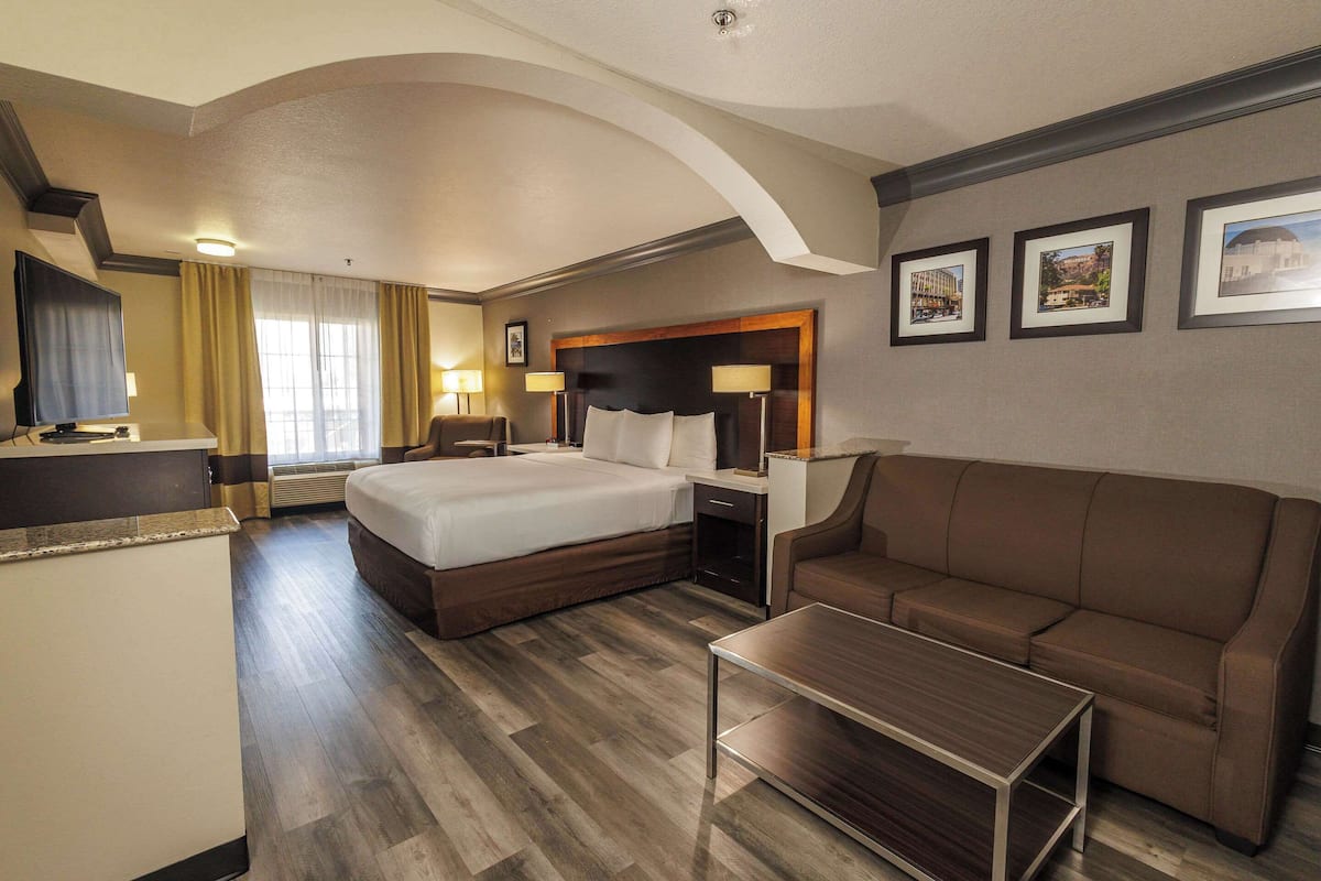 Une chambre d’hôtel avec un grand lit, un canapé, une petite table et un bureau avec une chaise. Il y a trois tableaux encadrés accrochés au mur.
