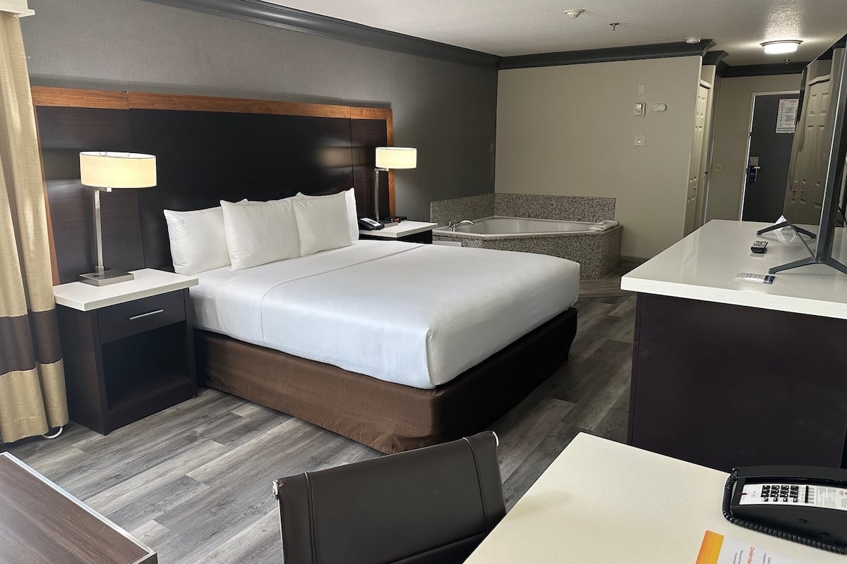 Une chambre d’hôtel avec un grand lit, des lampes de chevet, un bureau avec une chaise, une salle de bain avec une baignoire et un miroir.