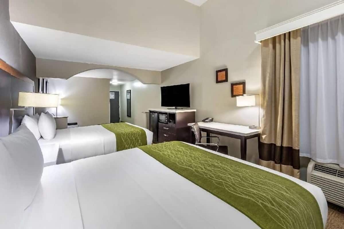 Une chambre d’hôtel avec deux lits, un bureau, une télévision et une fenêtre avec des rideaux.
