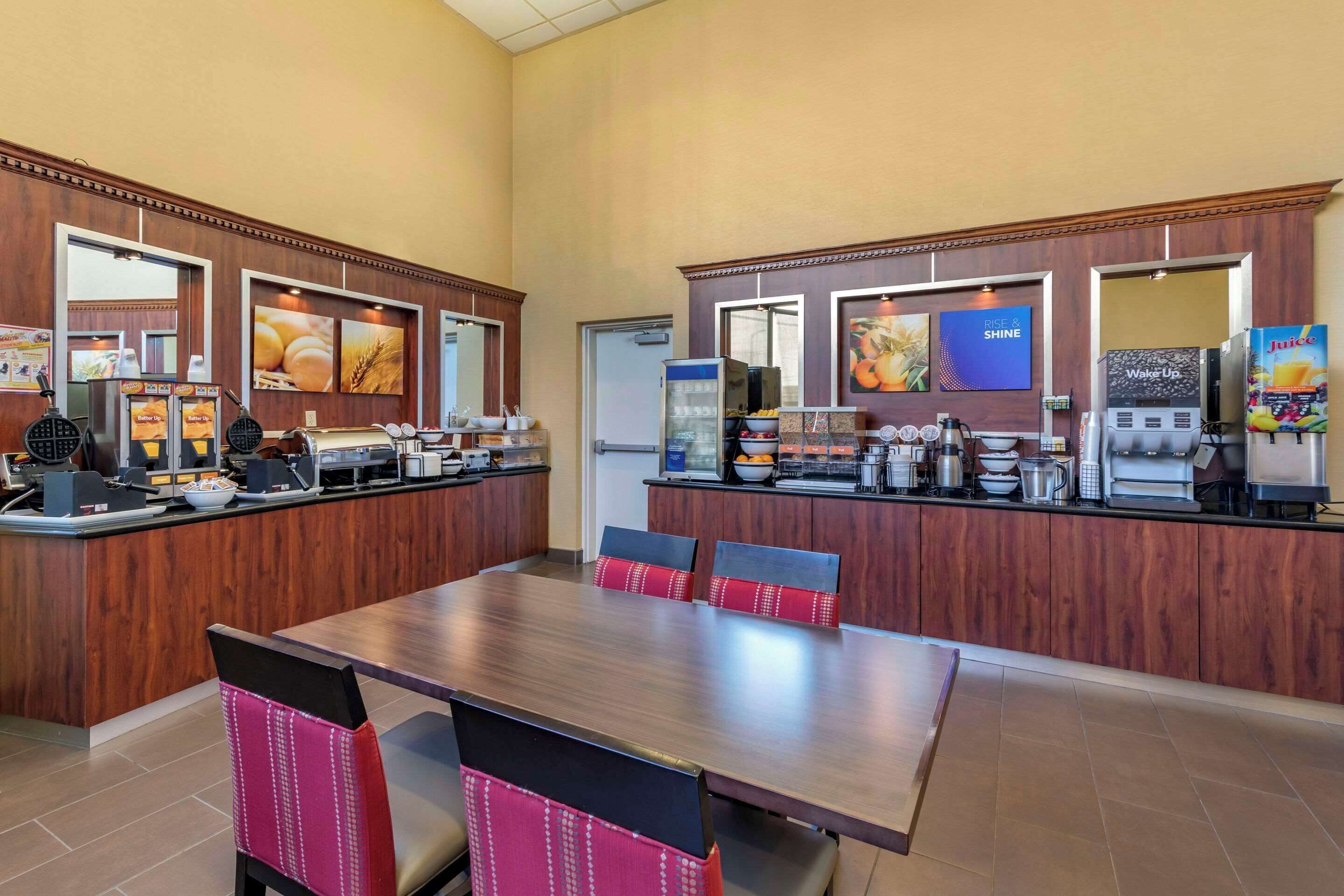 A hotel breakfast area with a wooden counter, seating, and various food and beverage machines.