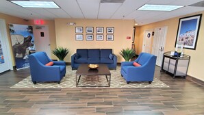 A lobby with blue armchairs, a central sofa, a coffee table, and framed pictures on the wall.