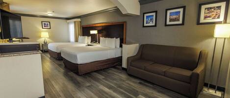 A hotel room with a large bed, a sofa, a desk, and a TV.