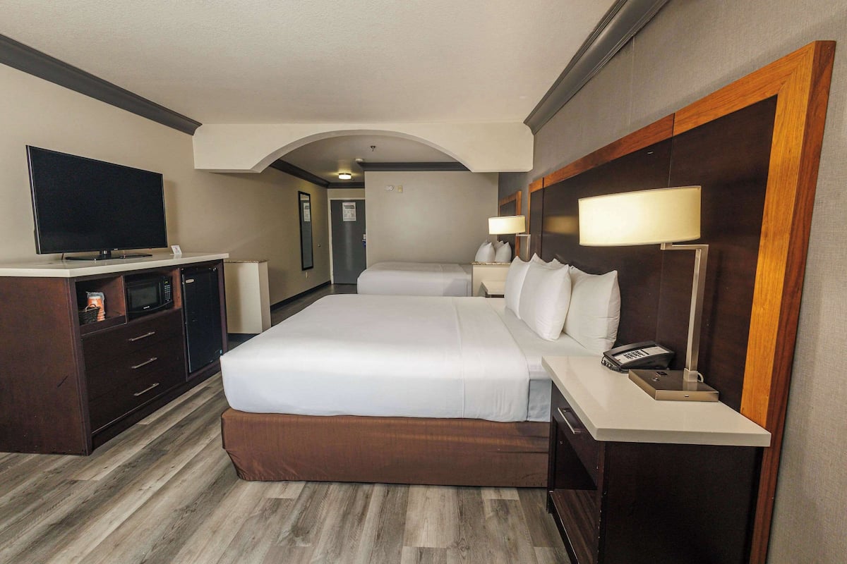 Une chambre d’hôtel avec un grand lit, une télévision, un bureau avec une lampe et une tête de lit en bois.