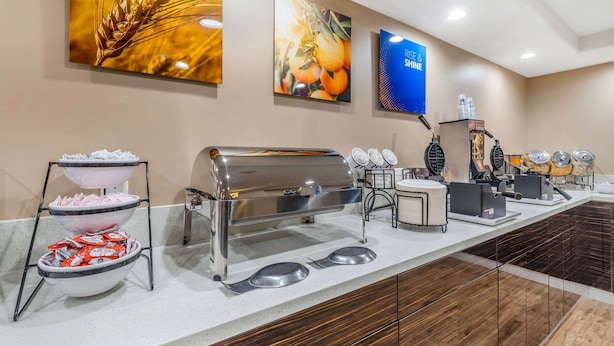 A buffet setup with a self-service grill, bowls of sliced fruits, and a beverage dispenser.