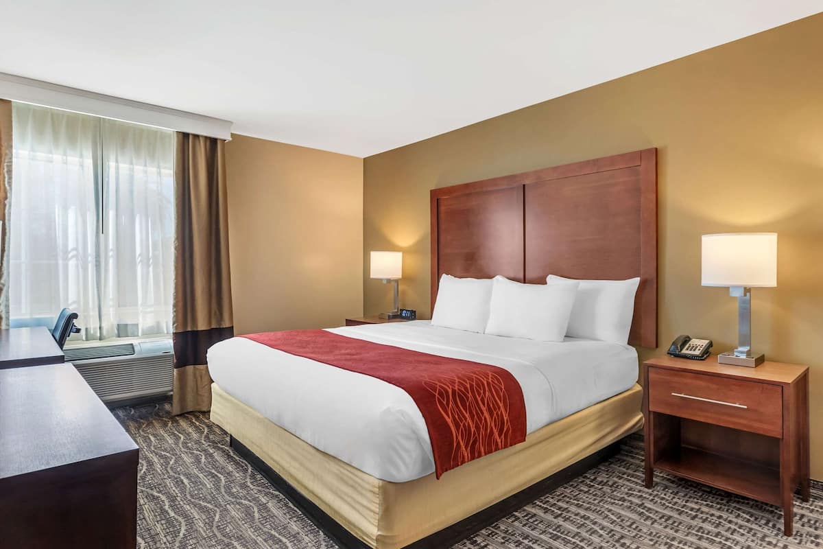 A hotel room with a large bed, two bedside tables with lamps, a desk, and a window with curtains.