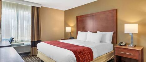 A hotel room with a large bed, two bedside tables with lamps, a desk, and a window with curtains.