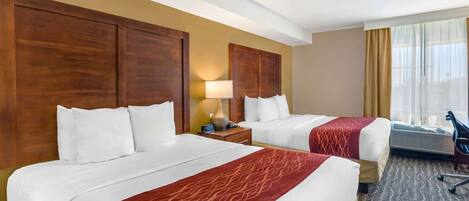A hotel room with two beds, a desk, a chair, and a window with curtains.