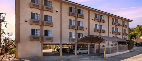A multi-story hotel with a flat facade, multiple balconies, and a covered parking area.
