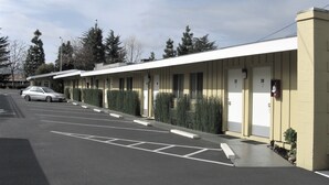 Une rangée de chambres de motel, chacune avec un numéro de porte distinct, un parking et une voiture garée devant.