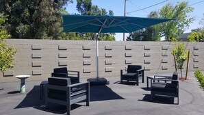 Un espace extérieur aménagé avec des sièges, un mur en briques, un parasol vert et plusieurs chaises noires.