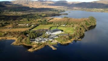 An aerial view of a lakeside property with a large building, surrounded by forested areas and hills in the background.