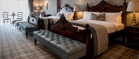 A hotel room with a large bed, a bench, two bedside tables, and a small table with chairs.
