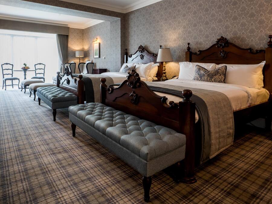 A hotel room with a large bed, a bench, two bedside tables, and a small table with chairs.