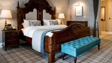 A classic four-poster bed with a tufted bench, two bedside tables with lamps, and a plaid carpet.