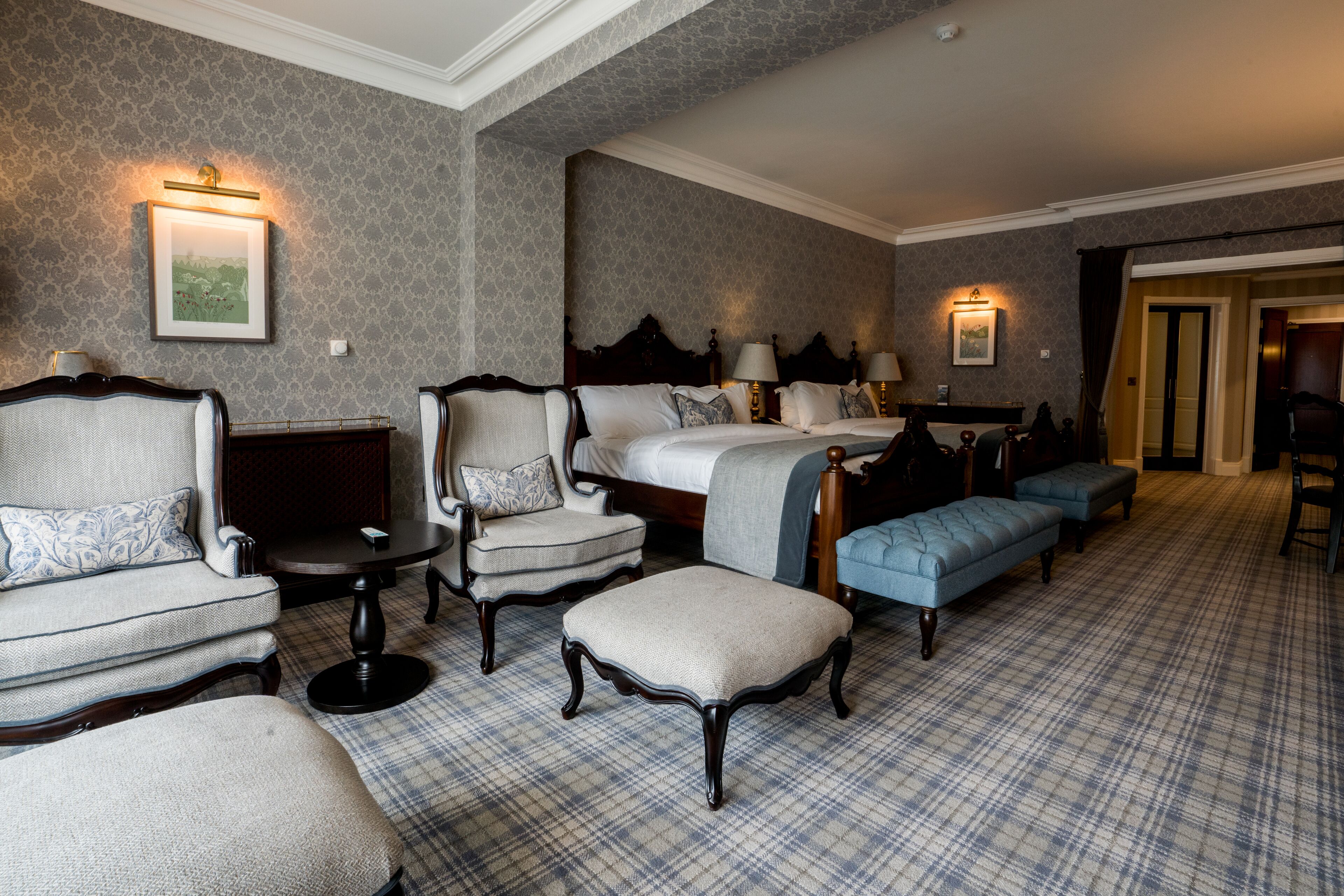 A hotel room with a large bed, two armchairs, a small table, and a blue sofa.