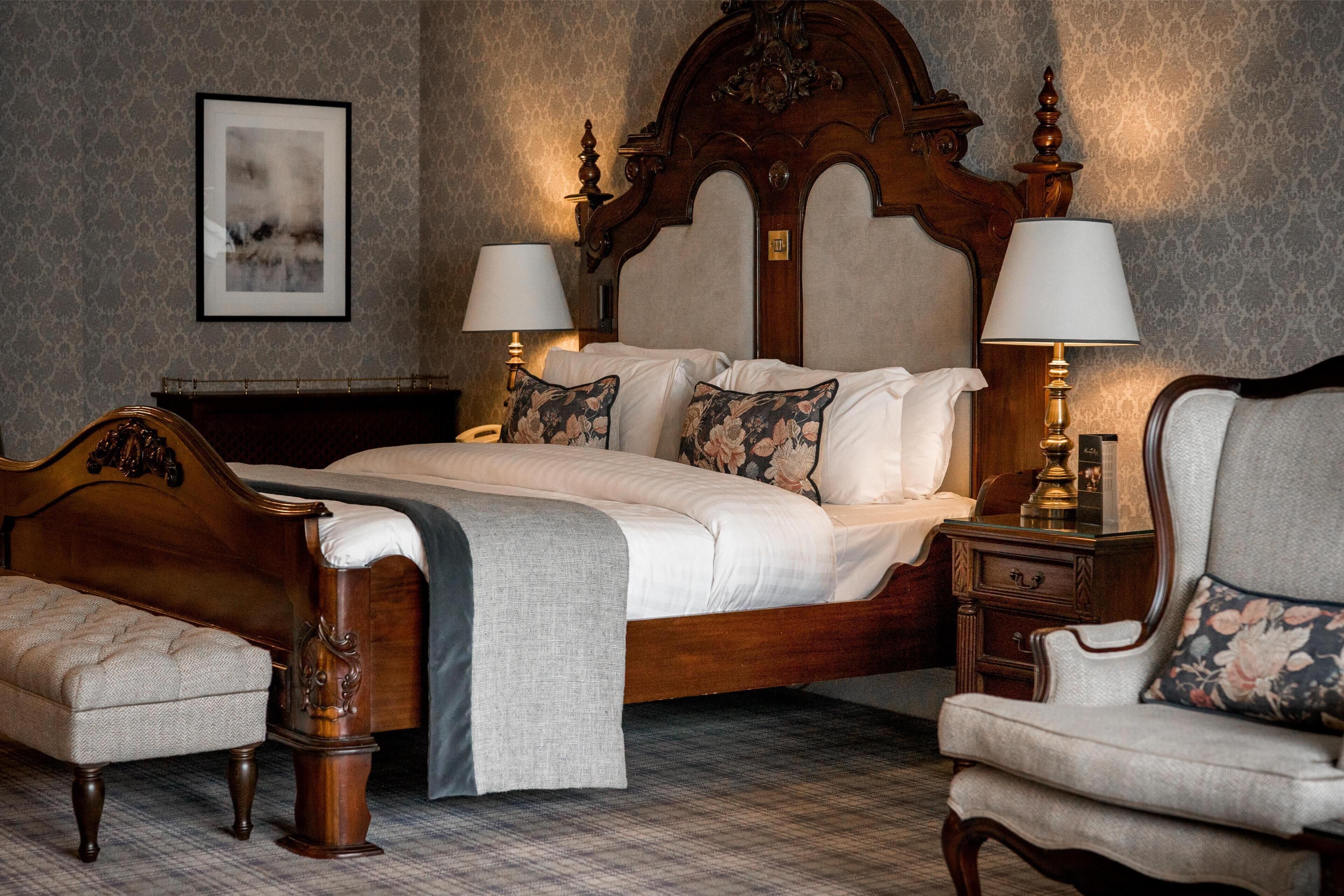 A hotel room with a large bed, two bedside tables, a chair, and a wooden headboard.