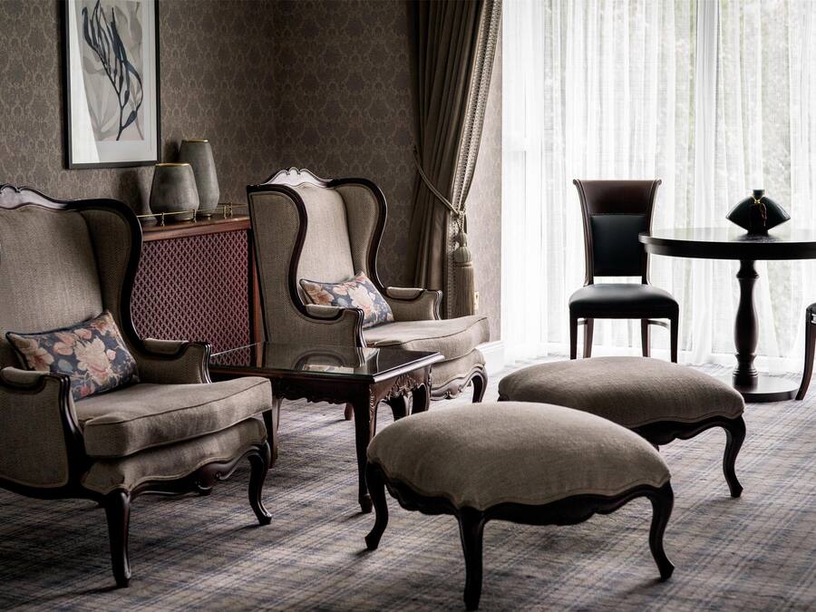 Een klassieke kamer met een kamerbreed tapijt, een zithoek, een bijzettafeltje en een ronde tafel met stoelen.