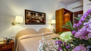 Een hotelkamer met een bed, bedlampjes, een schilderij aan de muur en een bloemstuk.