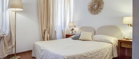 A neatly arranged bedroom with a bed, bedside tables, a lamp, and curtains.