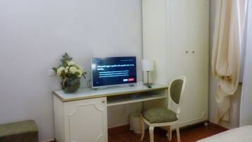 Ein Hotelzimmer mit Schreibtisch, Stuhl, Fernseher, einer Blumenvase und einem Kleiderschrank.