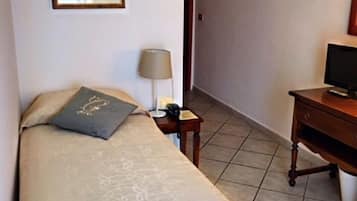 A hotel room with a bed, a bedside table with a lamp, a television on a wooden cabinet, and a framed picture on the wall.
