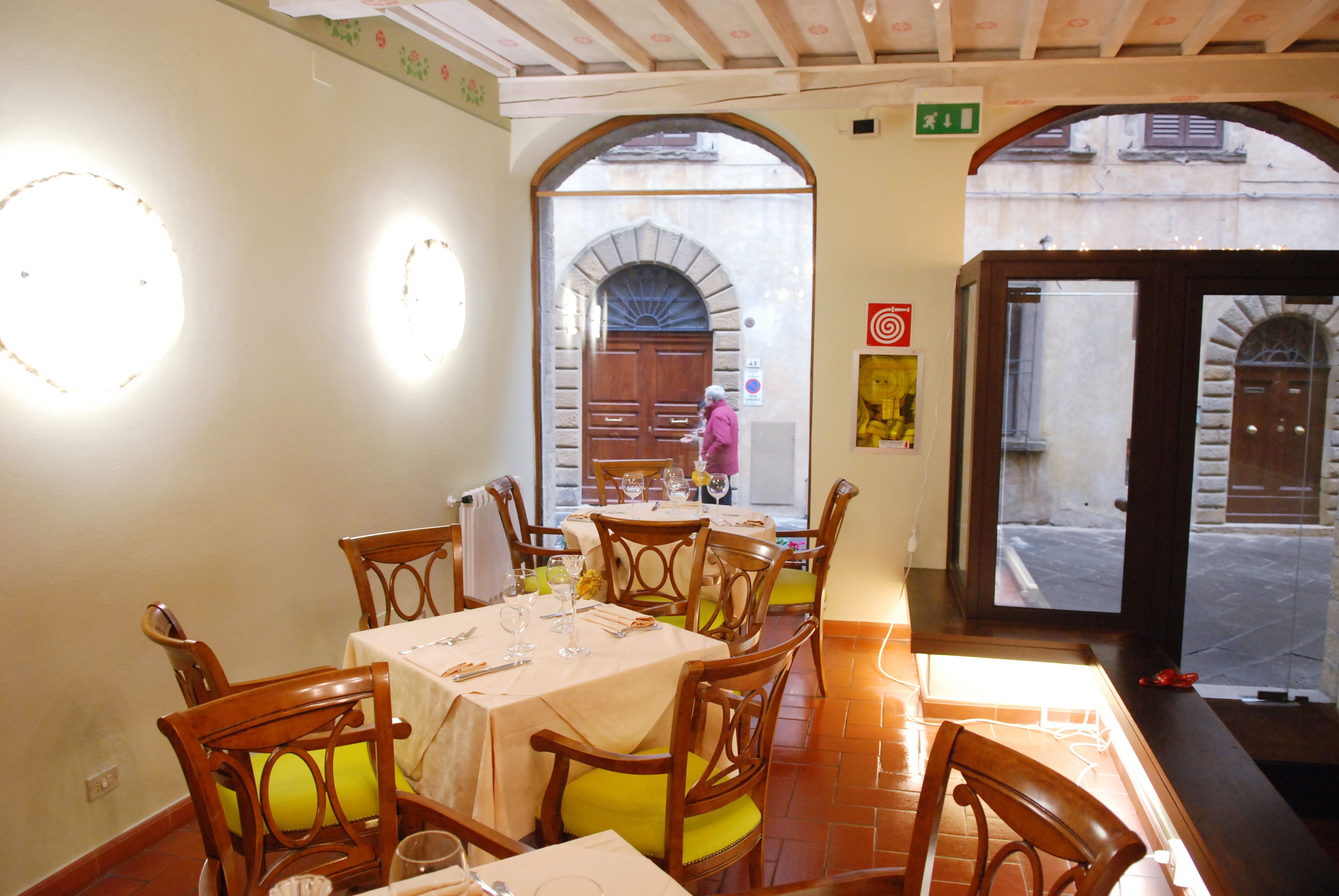 A dining area with wooden chairs and tables, a tiled floor, and a view through an arched doorway.