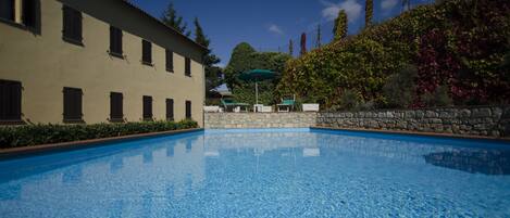 A swimming pool with a stone wall and a building with multiple windows.
