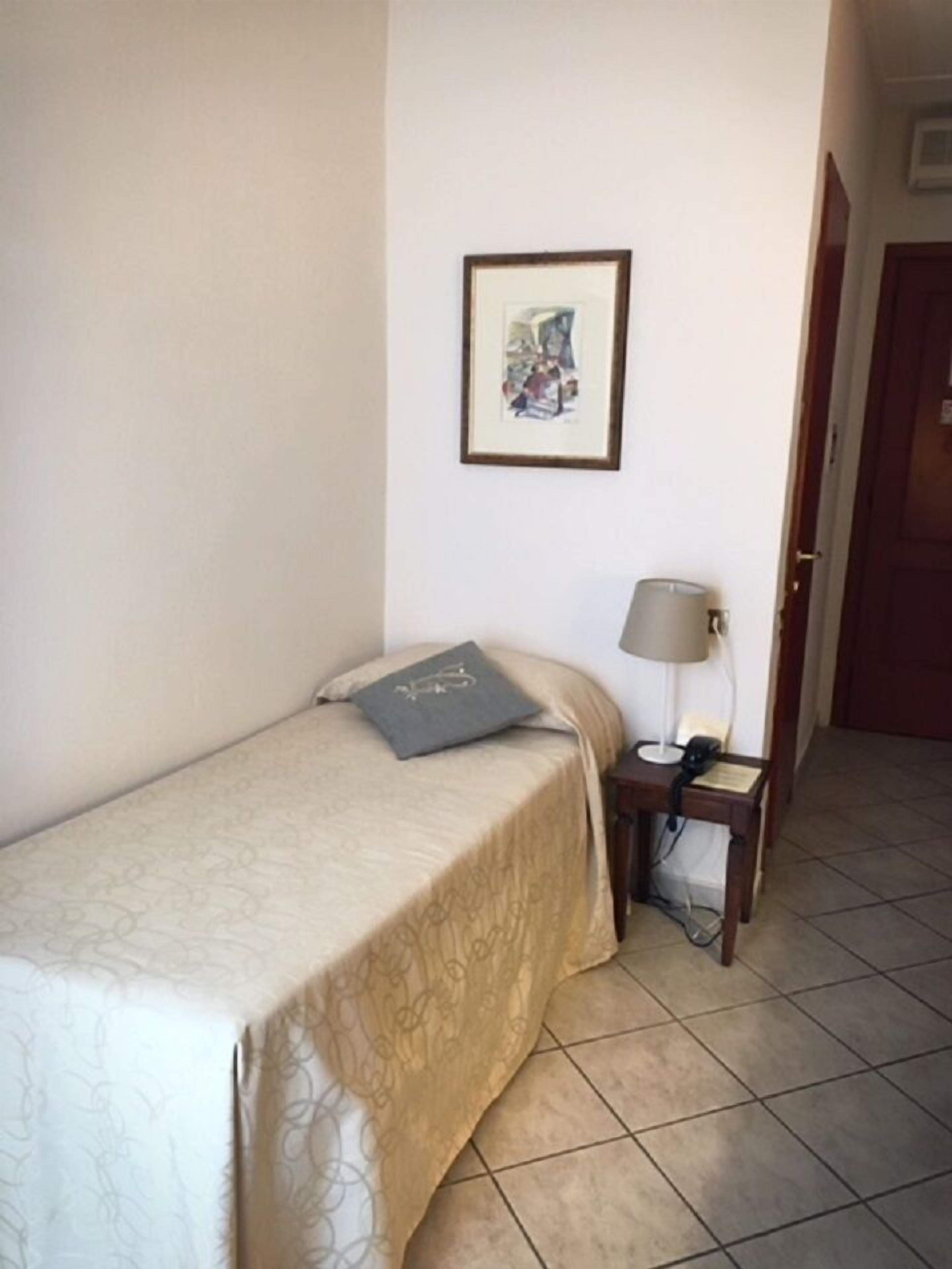 A single bed with a patterned bedspread, a bedside table with a lamp, and a framed picture on the wall.