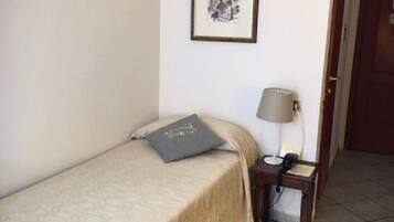 A single bed with a patterned bedspread, a bedside table with a lamp, and a framed picture on the wall.