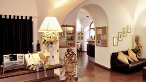 Un vestíbulo de hotel con un mostrador de recepción de madera, un sofá de cuero negro y un área de comedor al fondo.