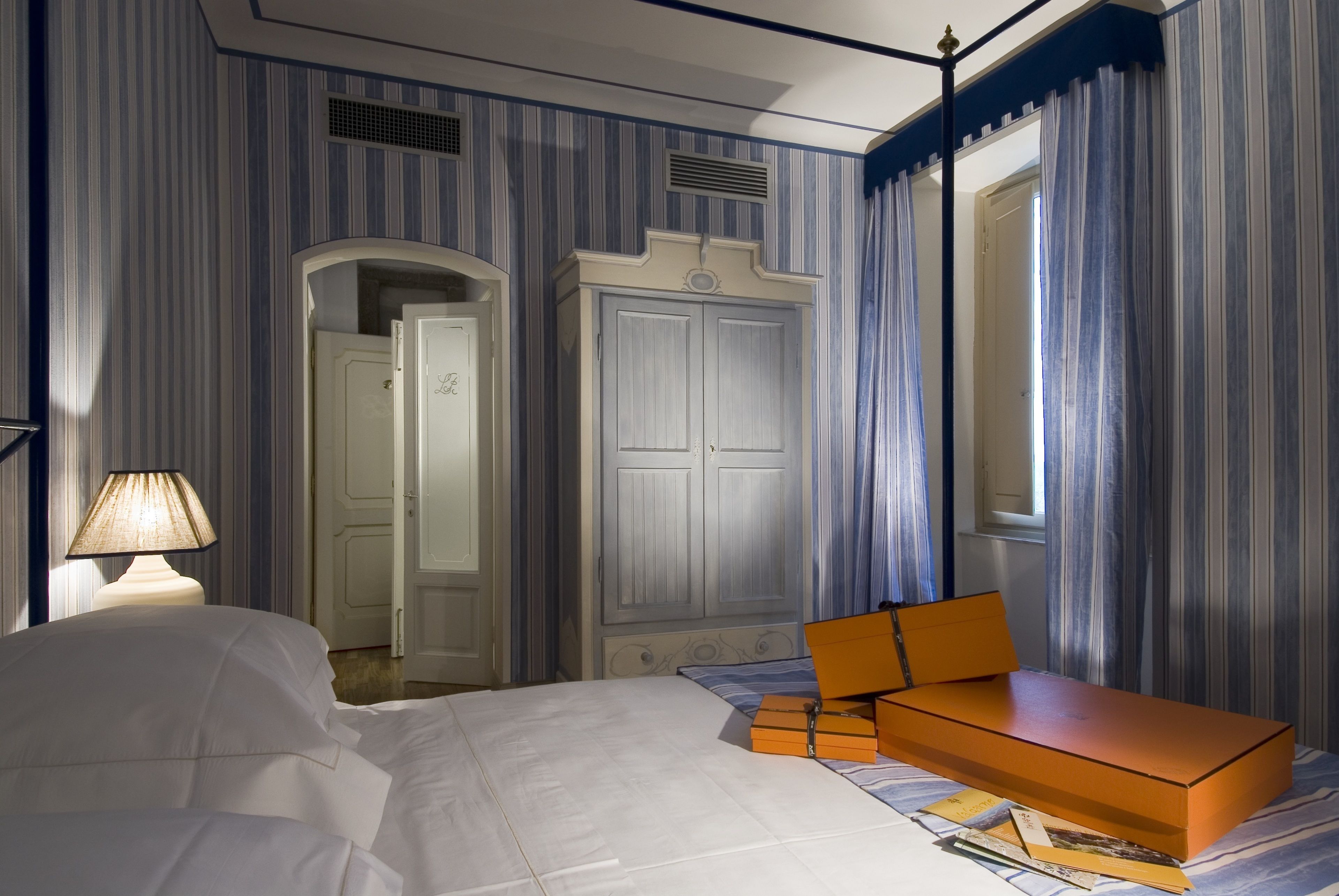 Una habitación de hotel con cama, escritorio, armario y ventana con cortinas.