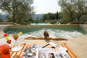 A poolside setting with a person relaxing, a table with drinks and magazines, and a view of the landscape. - Villa La Borghetta Resort (Figline e Incisa Valdarno)