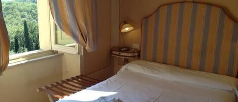 Une chambre d’hôtel avec un lit, une table de chevet, une lampe et une fenêtre avec des rideaux.
