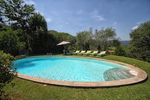 Una piscina con zona verde circundante, sillas de descanso y una pérgola.