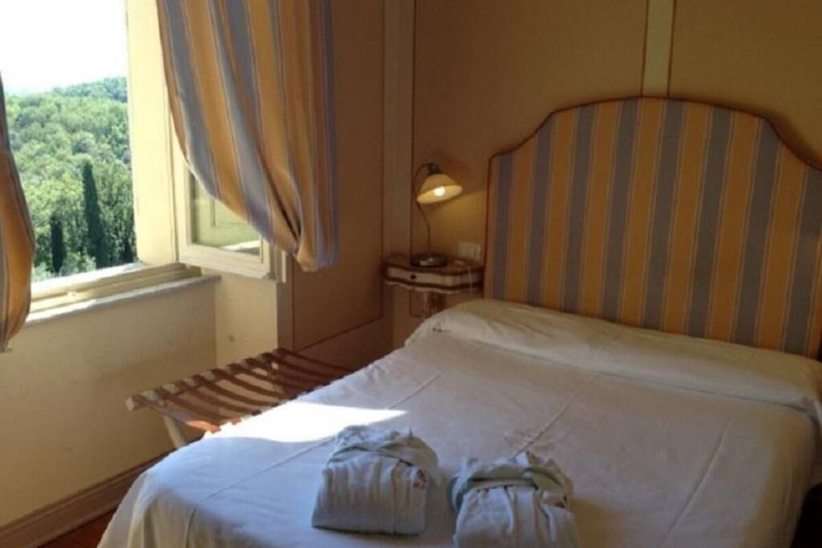 Habitación de hotel con cama, mesita de noche, lámpara y ventana con cortinas.
