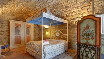 Un lit à baldaquin, une armoire en bois ornée d’une peinture florale et un mur en pierre.
