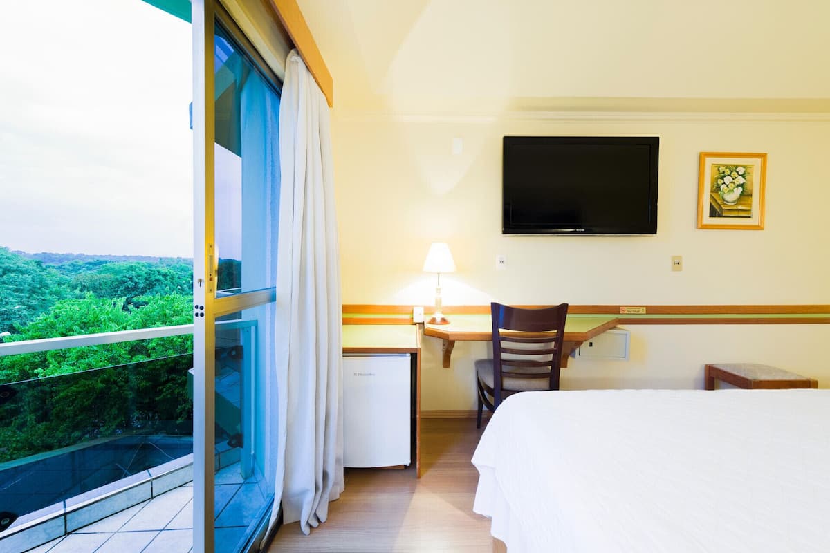 A hotel room with a bed, a desk, a chair, a TV, and a window with curtains.