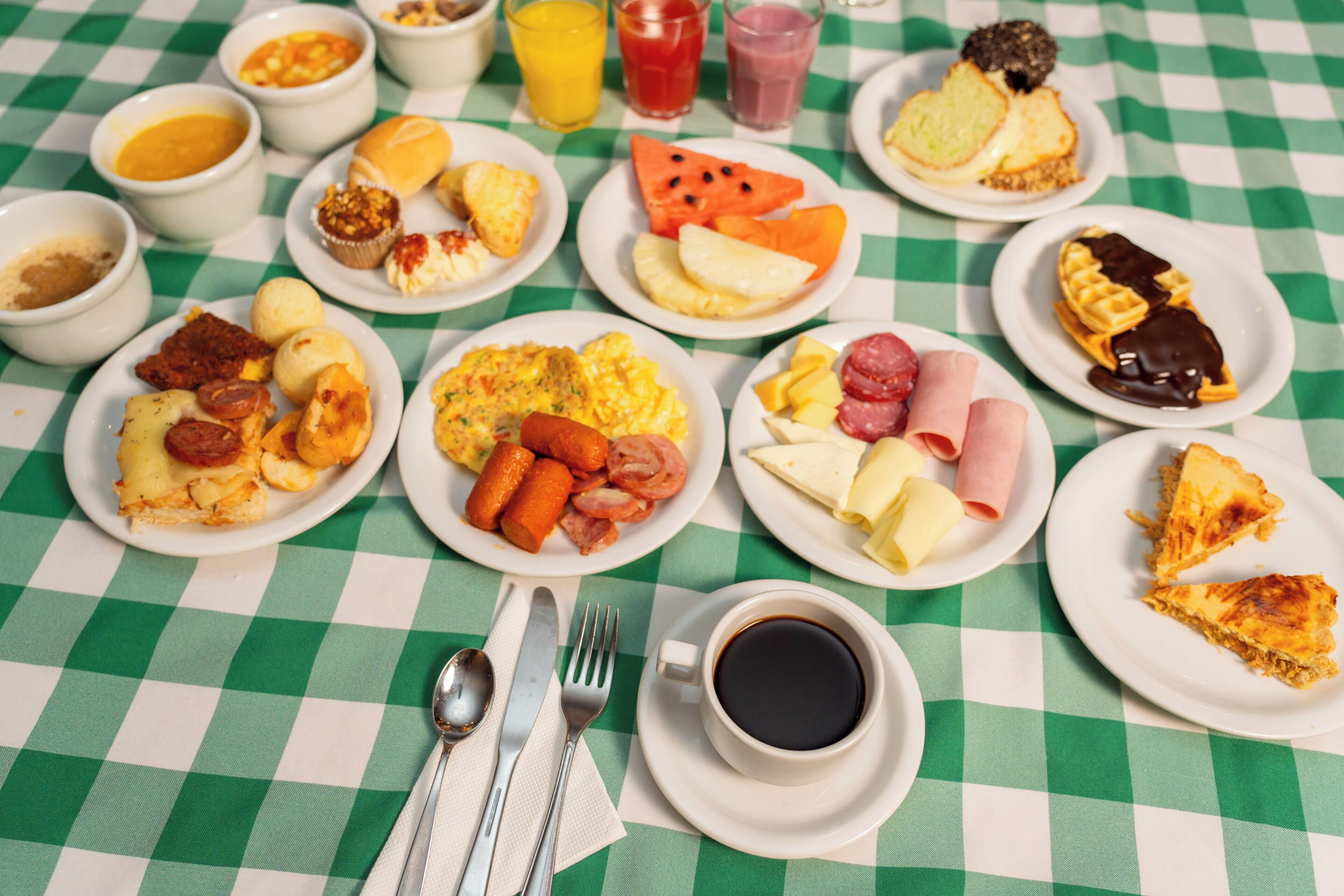 A table with various breakfast items including eggs, sausages, cheese, and a cup of coffee.
