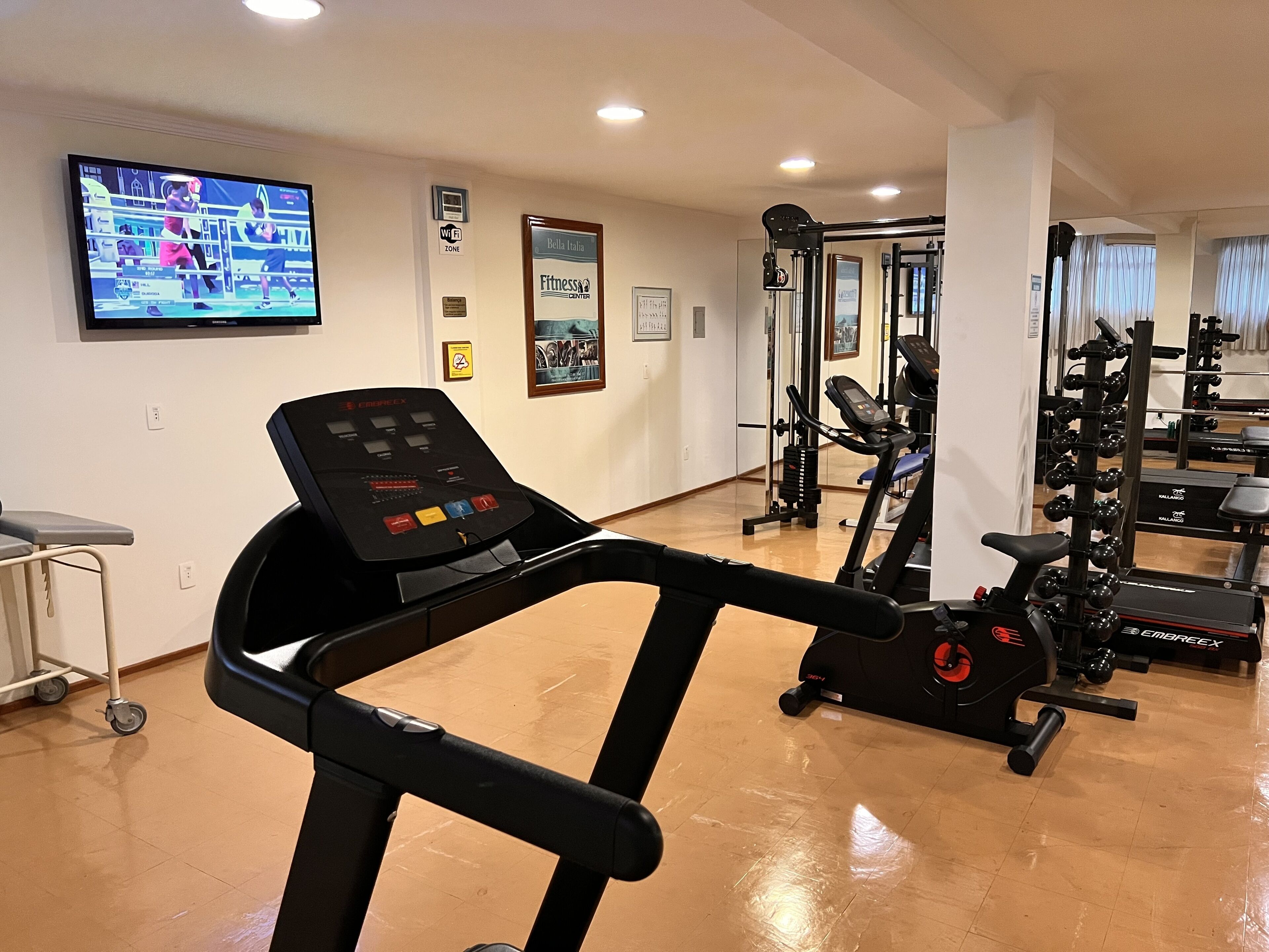 Une salle de sport équipée de matériel de cardio, d’un téléviseur diffusant un match de boxe et de divers panneaux d’information relatifs au centre de remise en forme.