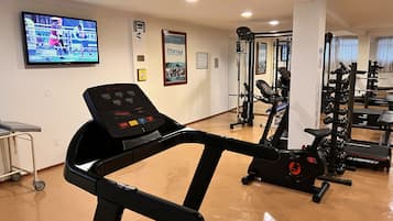 Une salle de sport équipée de matériel de cardio, d’un téléviseur diffusant un match de boxe et de divers panneaux d’information relatifs au centre de remise en forme.