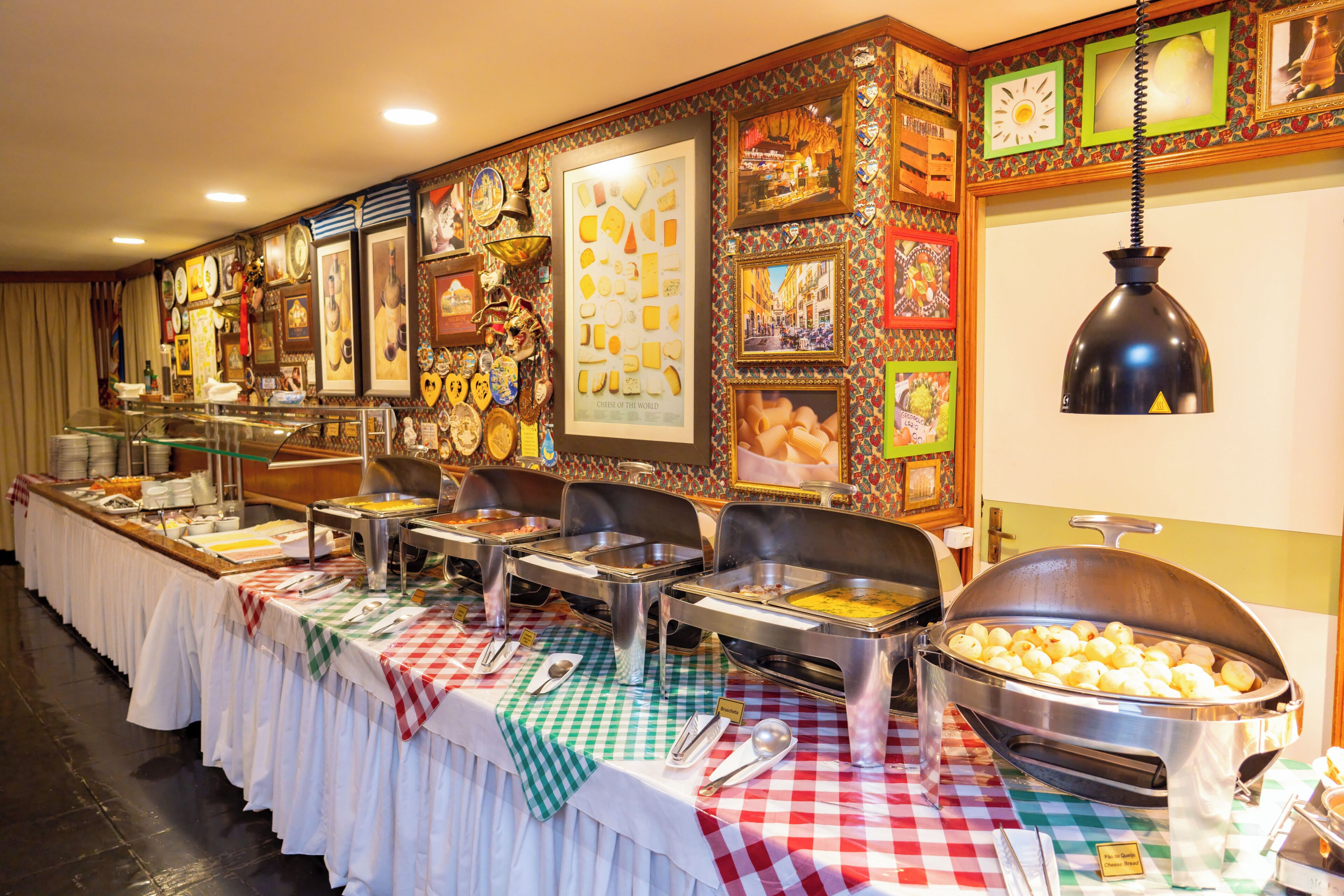 A buffet setup with various food stations, a checkered tablecloth, and a wall decorated with framed pictures and artifacts.