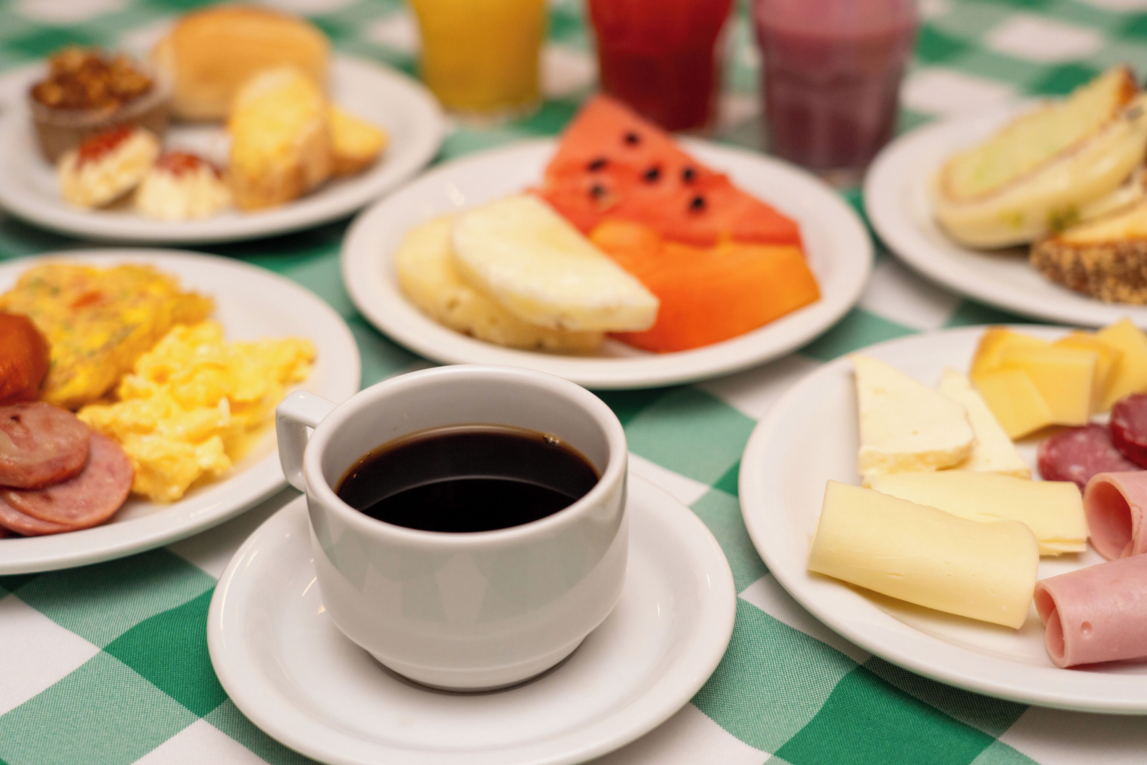 A breakfast table with plates of food, a cup of coffee, and a glass of juice.