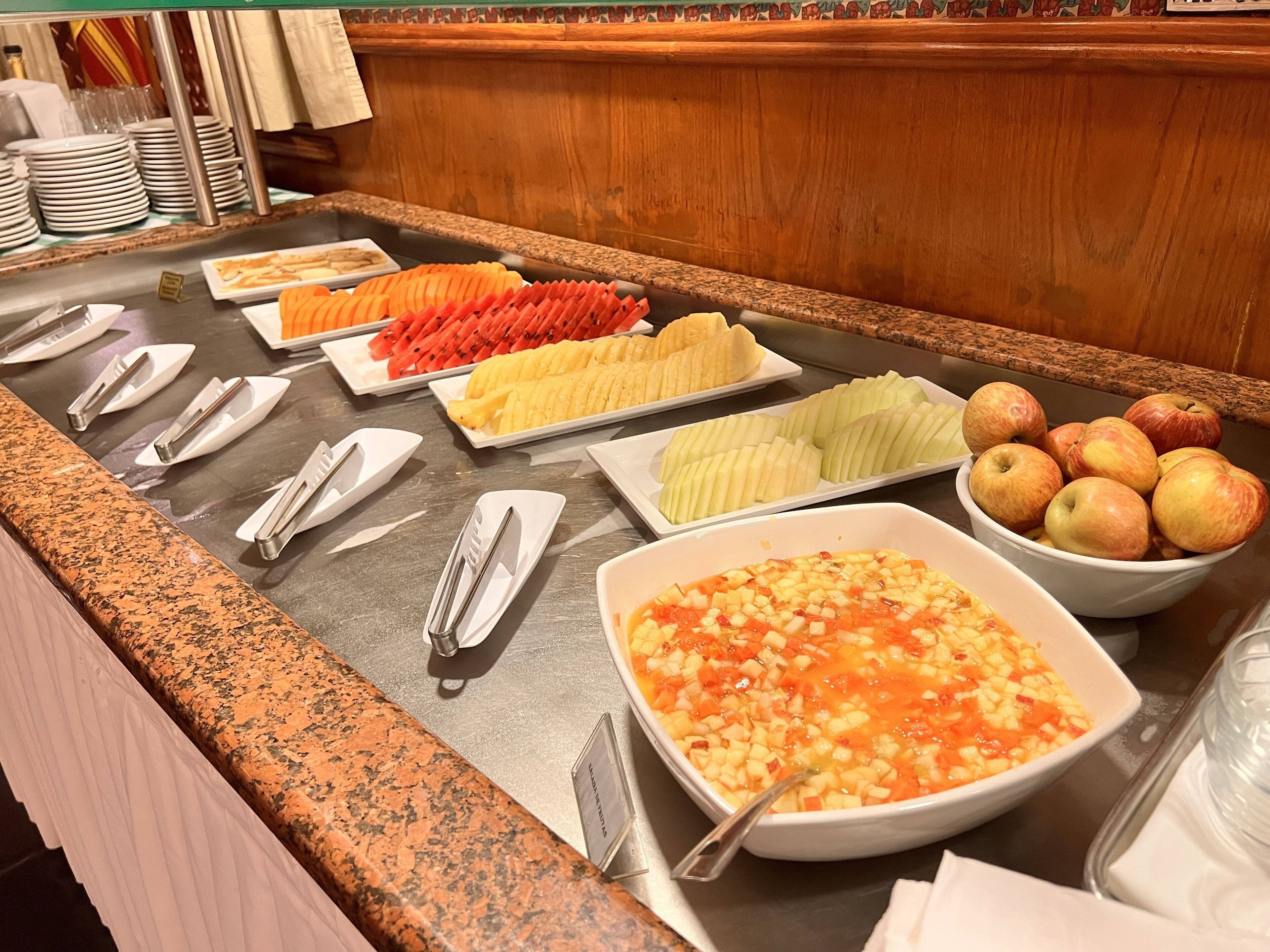 A buffet with various fruits and a bowl of diced fruit salad.
