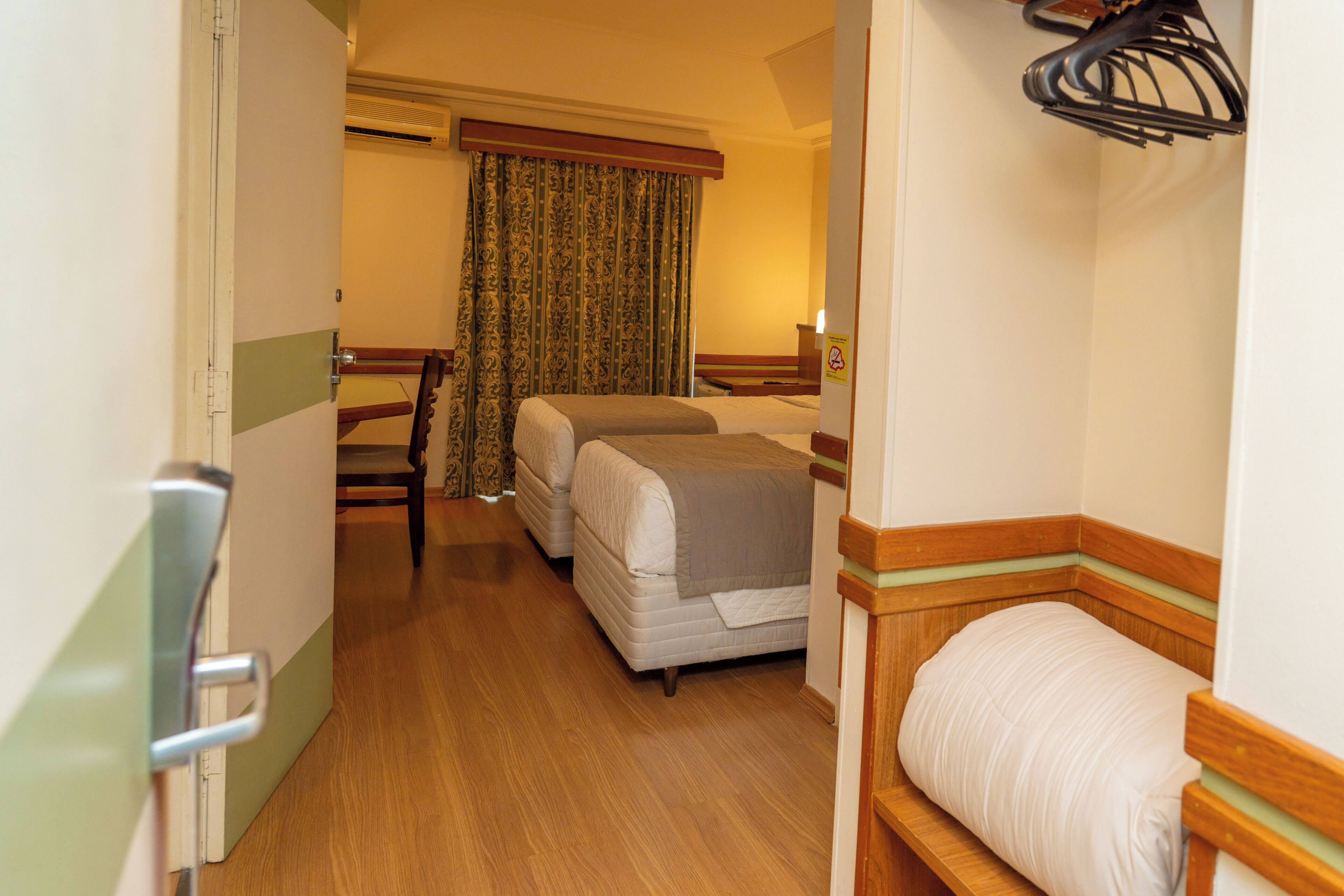A hotel room with two beds, a wooden floor, a chair, and a curtain.