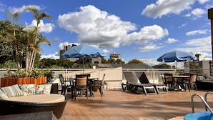 Un patio al aire libre con muebles de mimbre, sombrillas azules y vista a edificios al fondo.