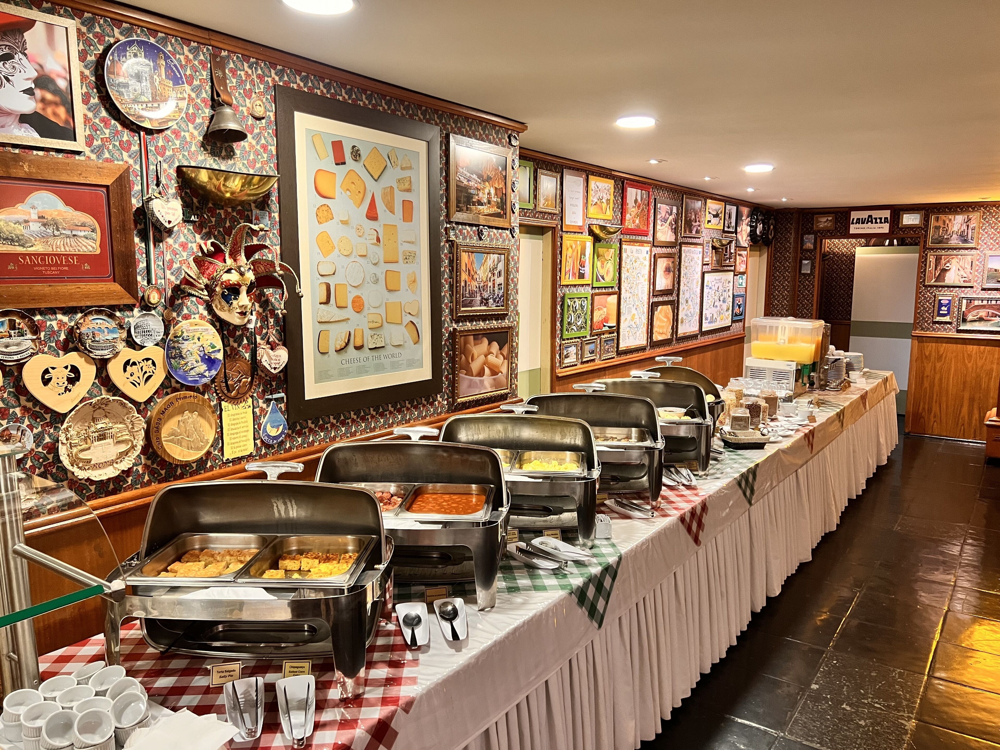 A buffet setup with various food stations, a wall decorated with cheese and travel-themed items, and a sign reading "Lavazza".
