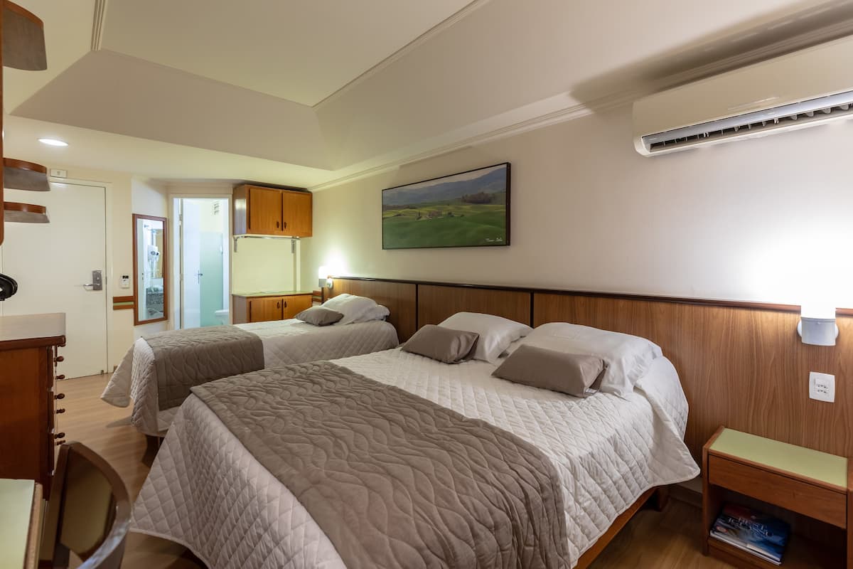 A hotel room with two beds, a wooden headboard, a painting on the wall, and an air conditioning unit.